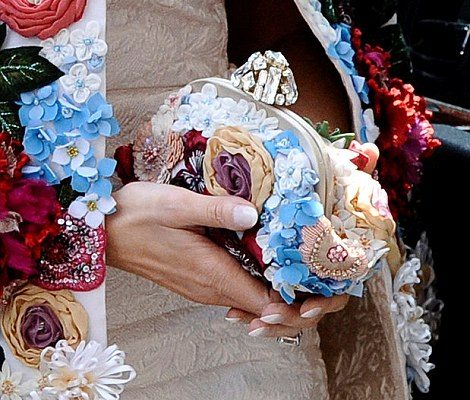 Melania Trump , esposa de Donald Trump, a porta do carro oficial. Ela usa um vestido , cor clara, e um casado com detalhes de flores 3D, de todas as cores. Ela usa óculos escuros. Em suas mãos uma bolsa pequena com os mesmo detalhes do casaco.